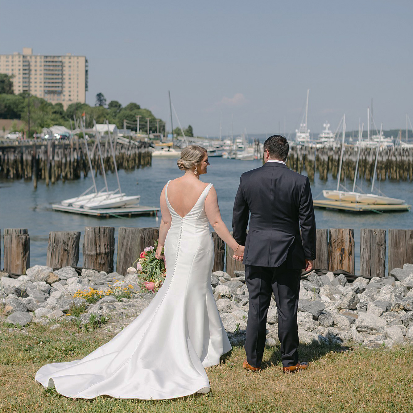 Bride and Groom hold hands as they overlook harbor in Portland Maine. Maine Wedding Deborah Zoe Photography