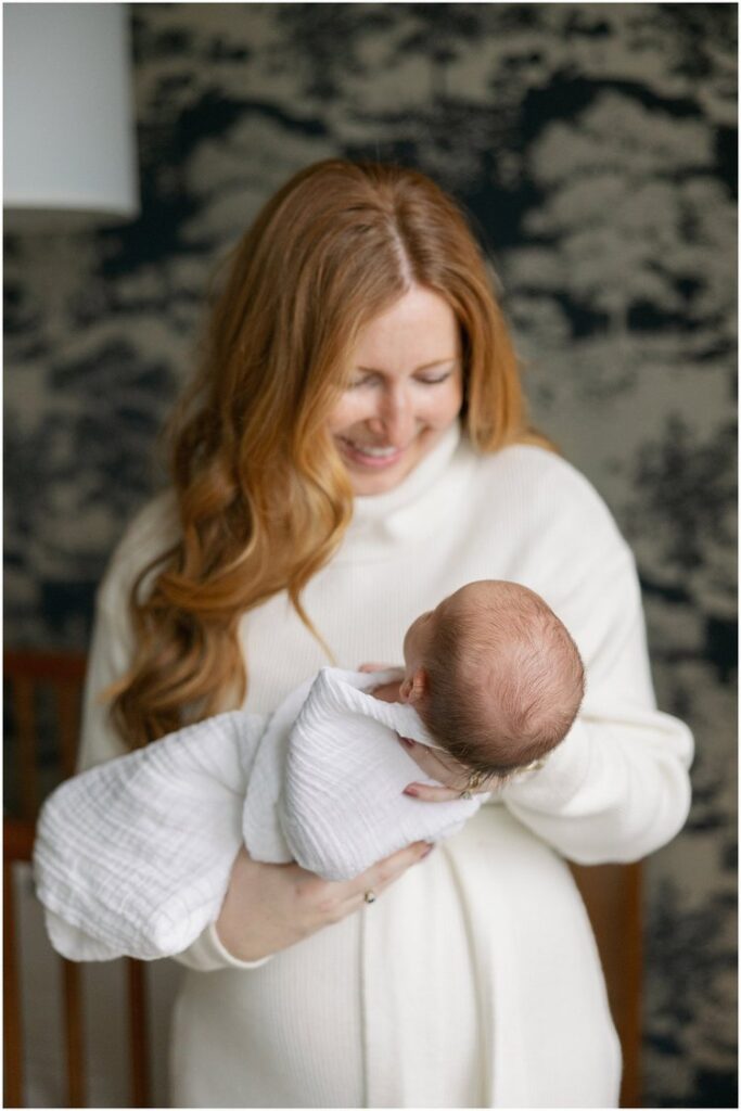 Mother with red hair smiles while holding newborn in her arms. Boston Newborn Session Deborah Zoe Photography.