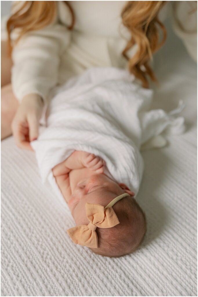 Women cradles swaddled baby on bed. Boston Newborn Photographer Deborah Zoe Photography.