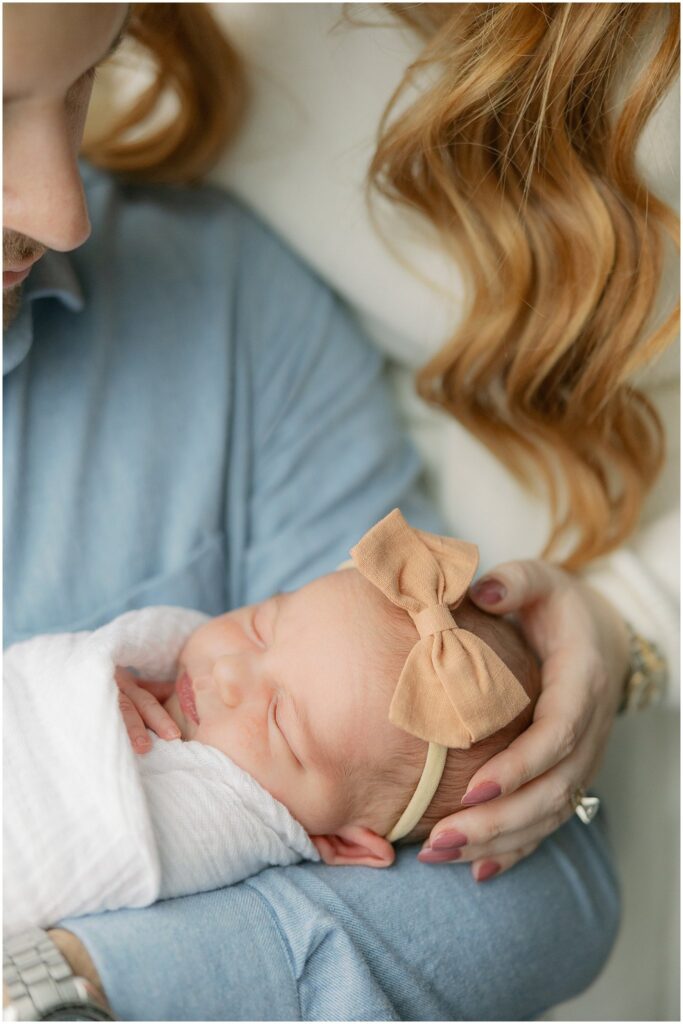 Close up of newborn baby with bow, in parent's arms. Boston Newborn Session Deborah Zoe Photography.
