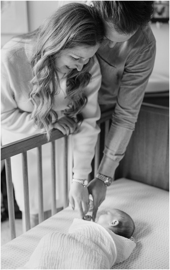 Mother and Father reach in crib to touch face of swaddled newborn. Boston Newborn Session Deborah Zoe Photography.