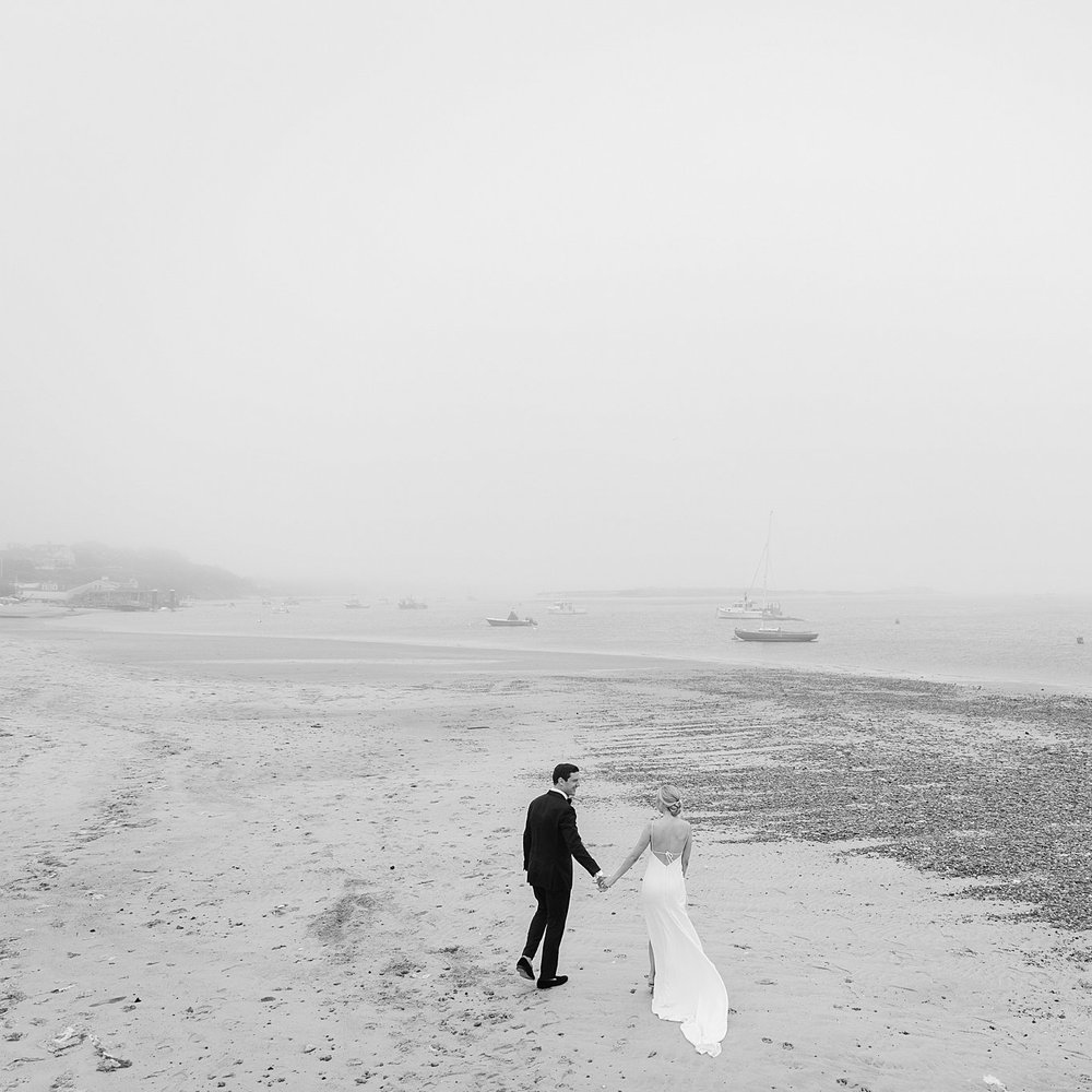 Black and white image of couple walking hand in hand on the beach during their wedding at Chatham Bars Inn. Deborah Zoe Photography.