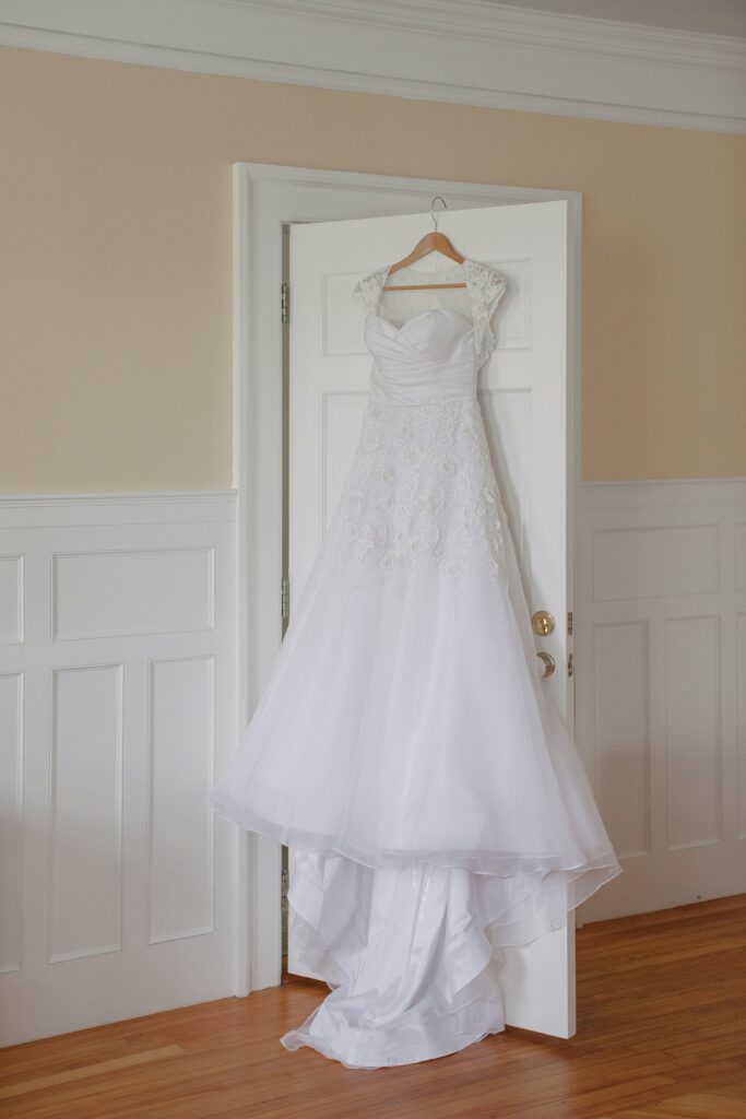 Wedding dress hangs on white door. Vermont Wedding Photographer Deborah Zoe Photography