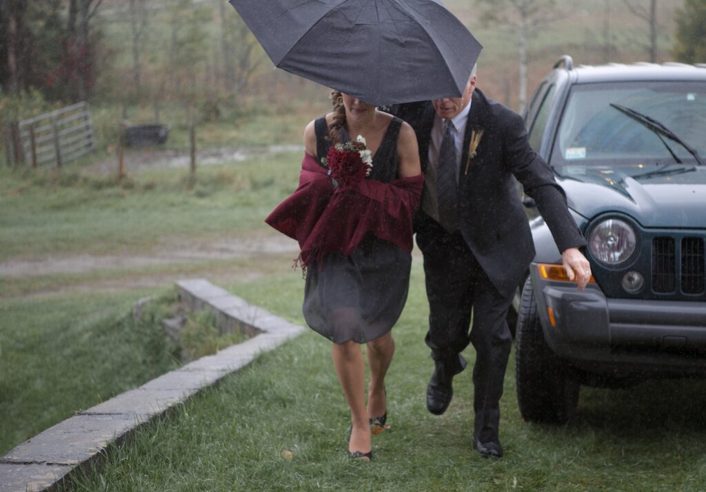 Guests walk into wedding ceremony under umbrella as it rains. Vermont Wedding Photographer Deborah Zoe Photography