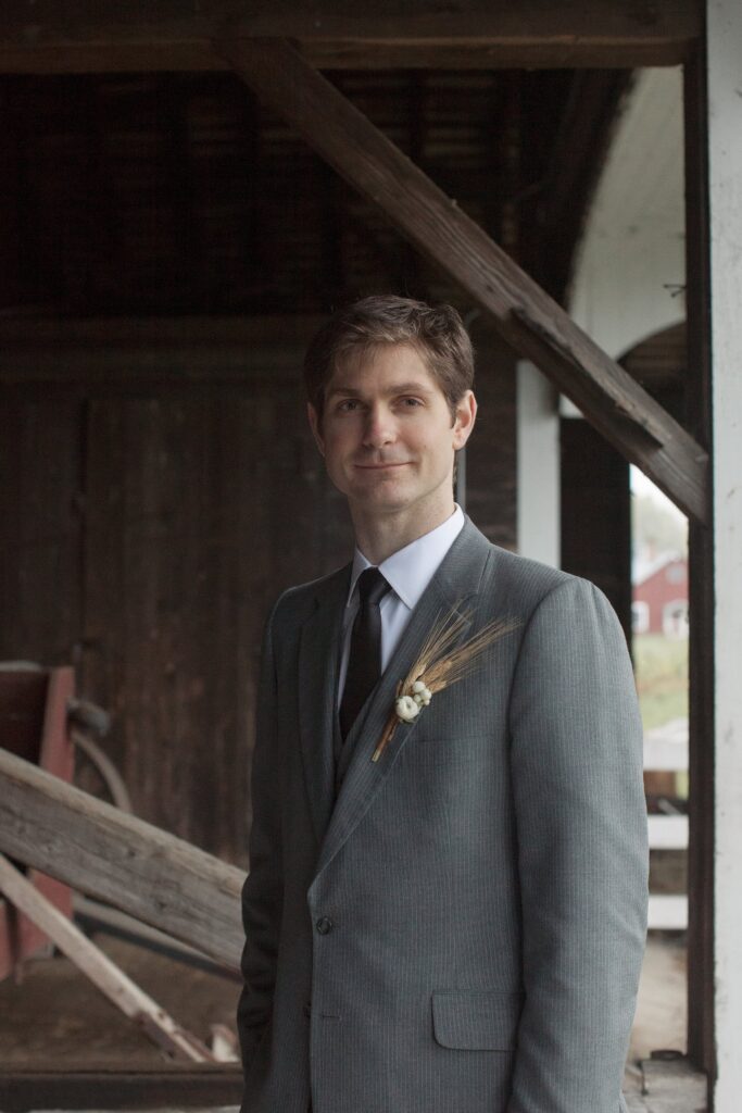 Portrait of groom wearing grey suit under over hang. Vermont Wedding Photographer Deborah Zoe Photography