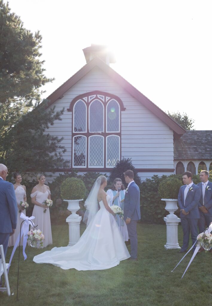 Bride and Groom hold hands during their outdoor ceremony in front of church. Coastal New England Wedding.