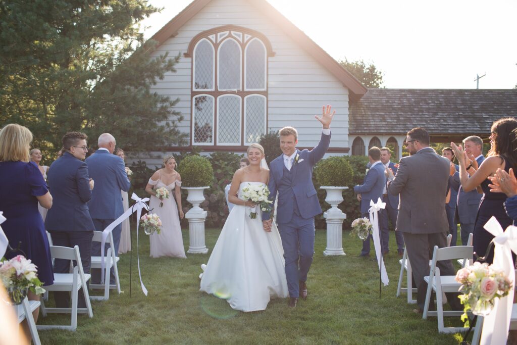 Bride and Groom celebrate as they walk down the aisle during their outdoor ceremony in front of church. Coastal New England Wedding.