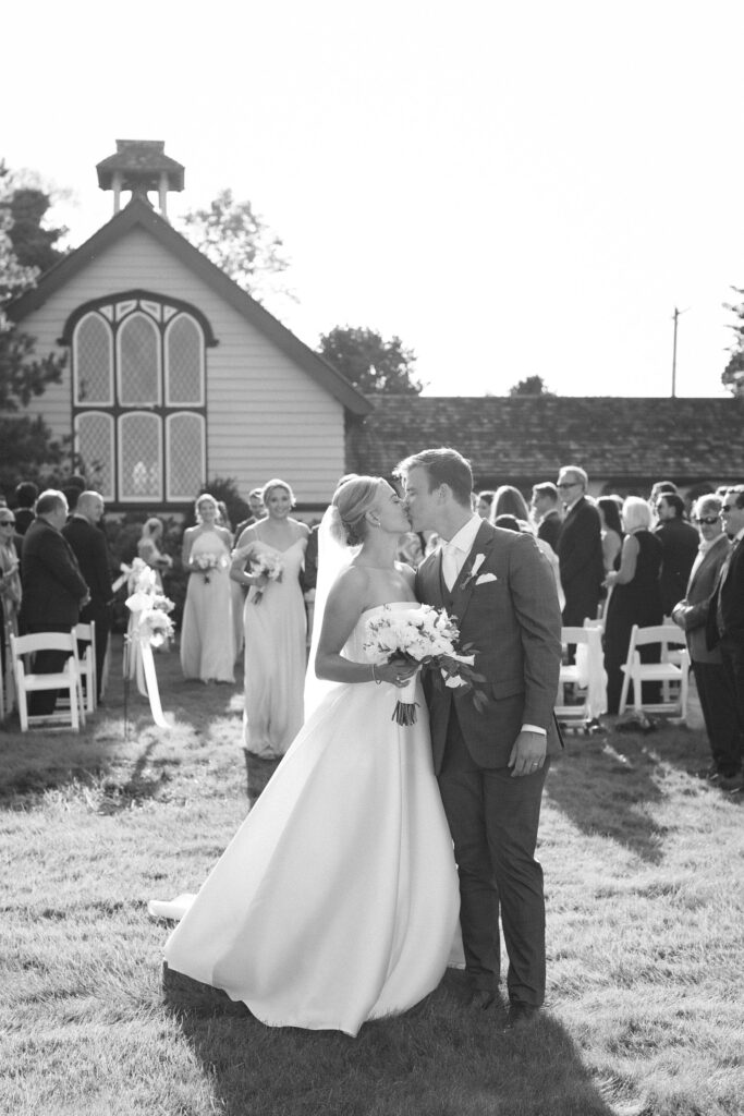 Bride and Groom kiss as they walk down the aisle during their outdoor ceremony in front of church. Coastal New England Wedding.