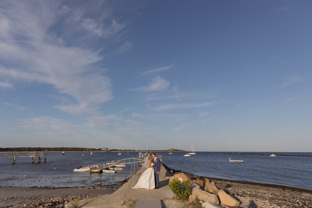 Bride and Groom pose together on a jetty with ocean behind them. Coastal New England Wedding.