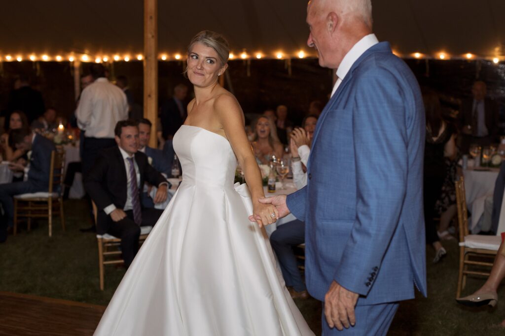 Bride looks back lovingly towards her father as they walk hand in hand onto the dancefloor. Coastal New England Wedding.