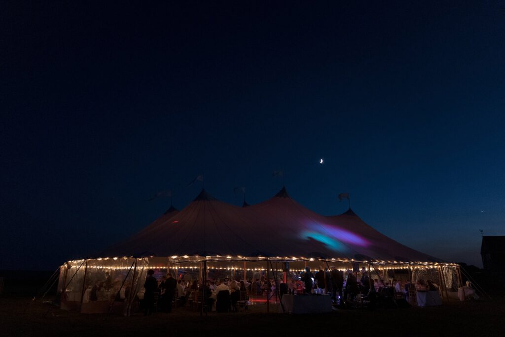 Sperry tent lit up at night with moon in the background during fall tented wedding reception. Coastal New England Wedding.