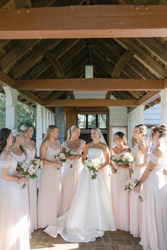 Bride surrounded by bridesmaids wearing pink dresses outside of church standing in entryway. Coastal New England Wedding.