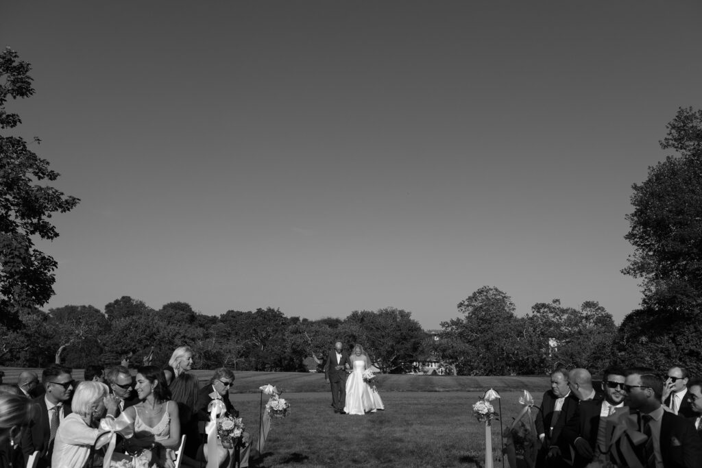 Bride walks down the aisle with her father in an outdoor ceremony in South Dartmouth. Coastal New England Wedding.