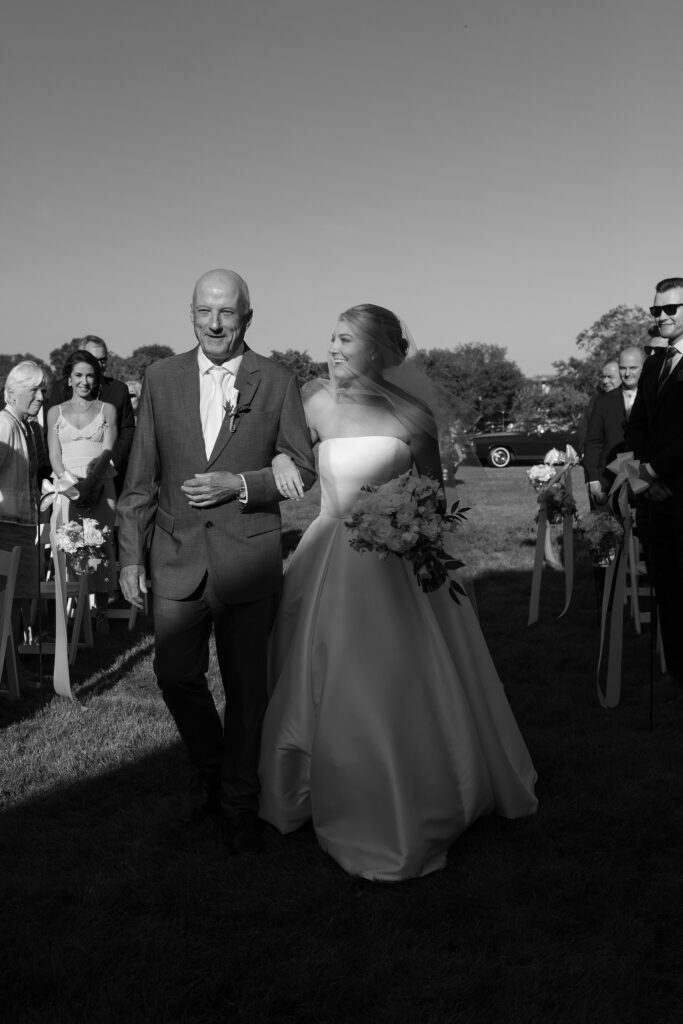 Bride walks down the aisle with her father in an outdoor ceremony in South Dartmouth. Coastal New England Wedding.