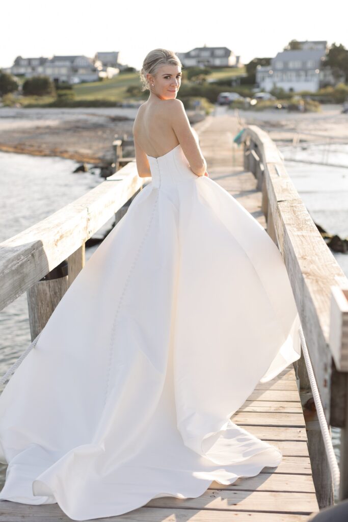 Bride poses on a jetty with ocean behind her. Coastal New England Wedding.