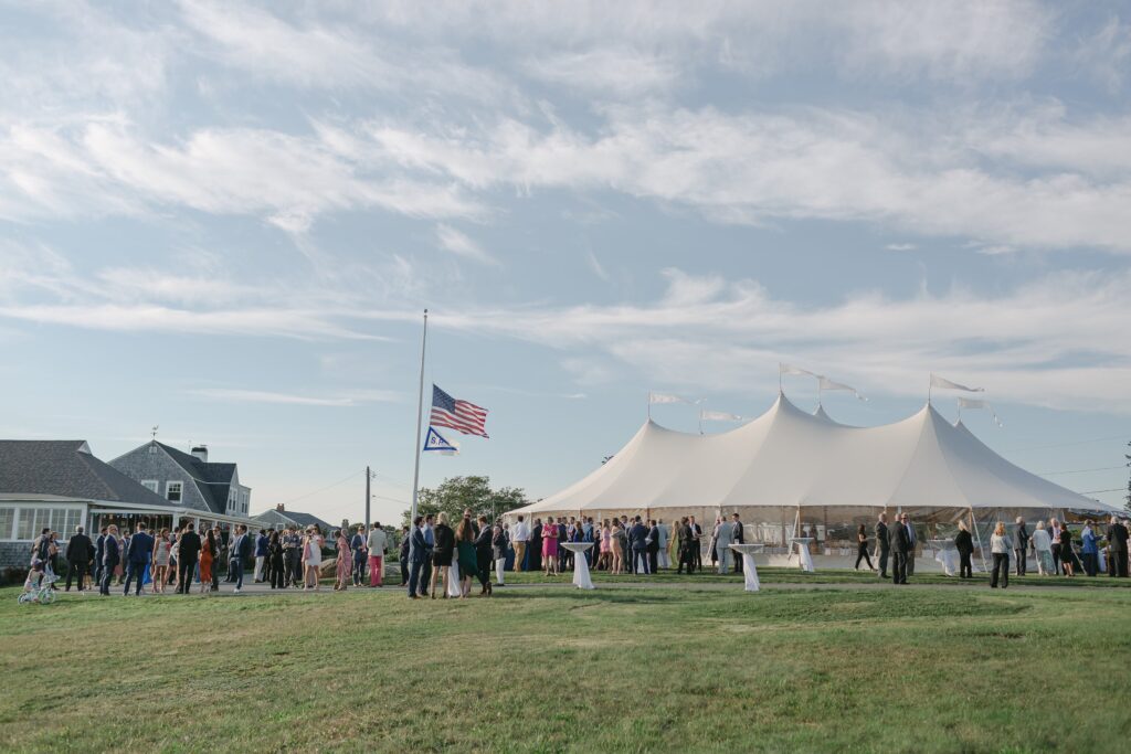 Landscape with guests enjoying cocktail hour outside with sperry reception tent behind them. Coastal New England Wedding.